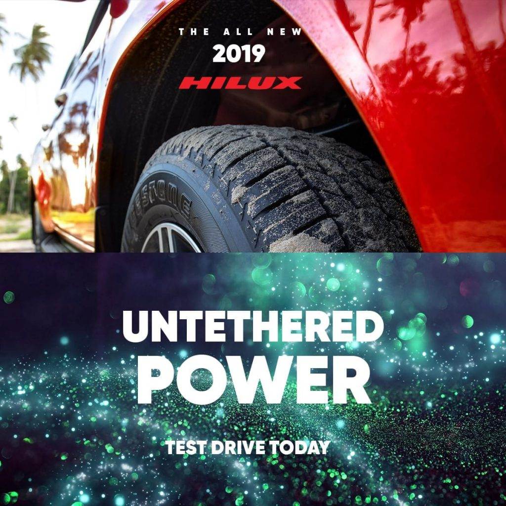 Close-up of a car wheel and body of a red 2019 Hilux. Text below reads: "Untethered Power. Test drive today" on a glittery background, crafted by your trusted Caribbean Advertising Agency in Trinidad and Tobago.