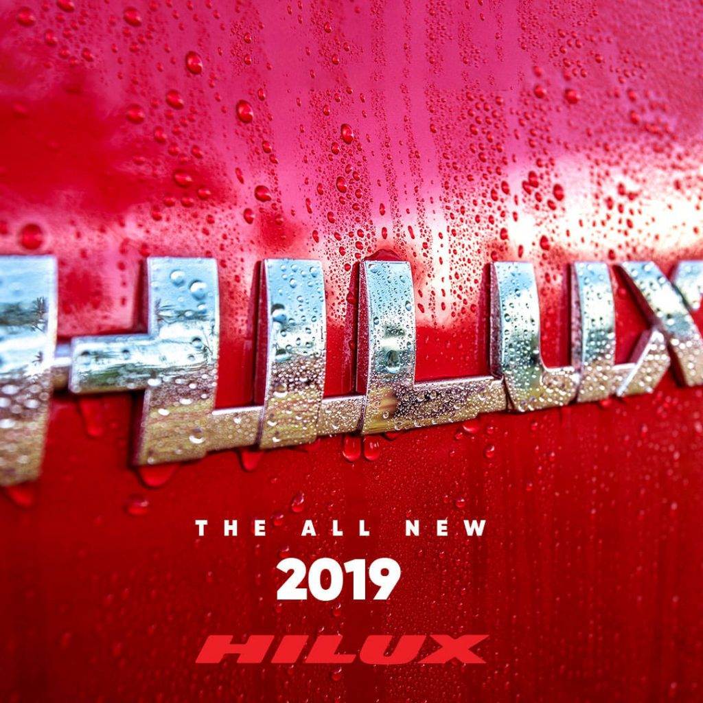 Close-up of a red 2019 Hilux with water droplets glistening on the surface and the silver Hilux logo prominently displayed—a stunning visual ideal for a Caribbean Advertising Agency in Trinidad and Tobago, capturing the essence of regional appeal.